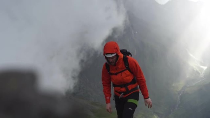 一名男性徒步旅行者带着雨具爬上岩石山腰的特写镜头