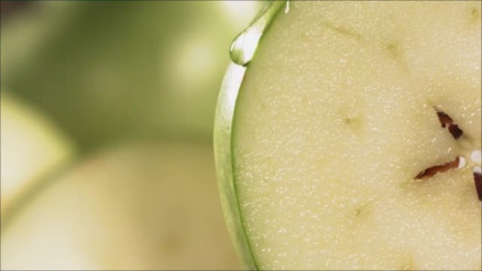 一滴水顺着成熟多汁的青苹果片的表面流下来。慢动作4K