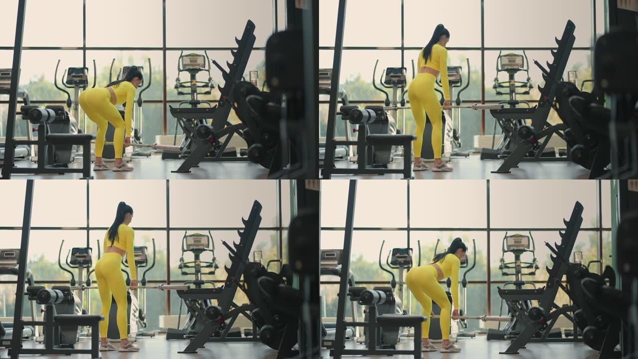 适合西班牙裔女性穿着黄色运动服在健身房用杠铃进行举重硬拉运动。女人黑发健身表演和杠铃做硬拉运动