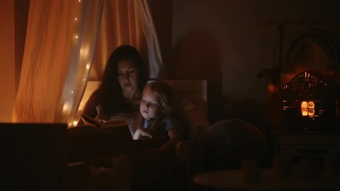 细心的母亲在睡前为小女儿读童话故事，女人正在与孩子共度时光
