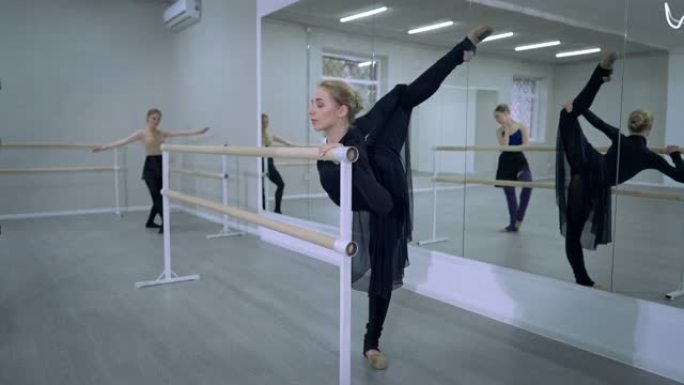 优雅美丽的芭蕾舞演员在舞蹈工作室排练蔓藤花纹，芭蕾舞演员在背景。自信的白人年轻女子练习古典芭蕾舞动作
