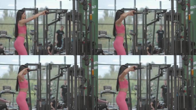 一个穿着粉红色西装的黑发女人将跨界训练器中的绳子拉到她的胸前。在教练中进行背部锻炼。专业女性教练