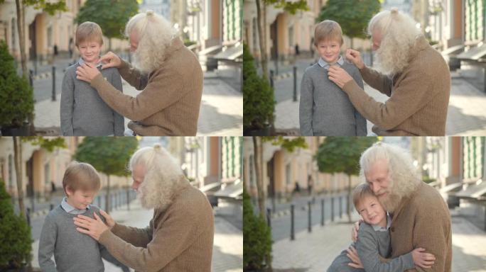 关心白人的老人在城市街道上调整微笑小男孩的衬衫。感激的孙子拥抱祖父离开。阳光明媚的户外快乐的祖父母和