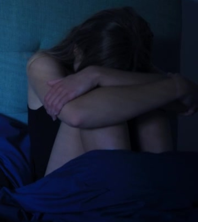 躺在床上的女人在恐惧或悲伤中拥抱膝盖