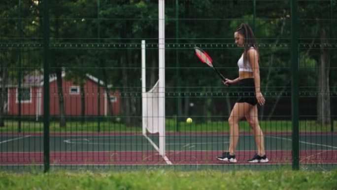 黑发网球运动员正在球场上散步，弹跳球，穿着短裙的苗条运动女人
