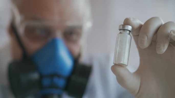 一位戴着蓝色呼吸器和防护眼镜的科学家的极端特写镜头，他开发了一种装有白色粉末安瓿的冠状病毒疫苗。麻醉