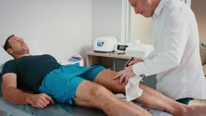 整形外科医生在手术前咨询期间剃刮患者的膝盖。运动相关的腿部受伤后躺在医院的病床上。医生为病人准备手术
