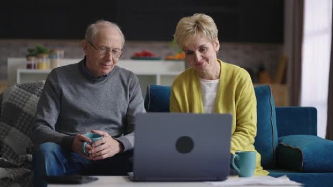 老年已婚夫妇通过笔记本电脑与朋友或家人进行视频聊天，周末在家休息