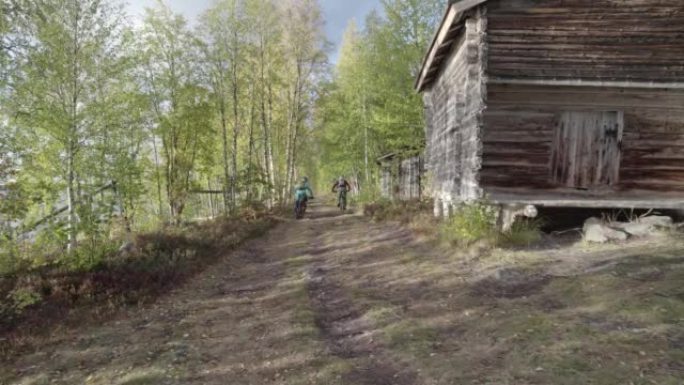 空中无人机拍摄了一对山地自行车夫妇在小屋附近的树林中行驶的路径