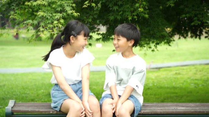微笑的小学男孩和女孩坐在公园的长凳上
