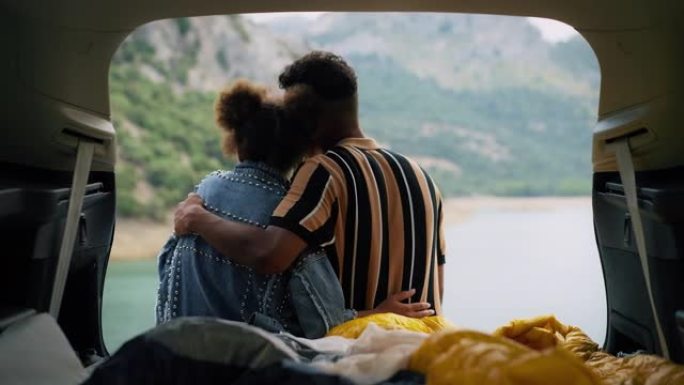 非洲族裔情侣坐在一起，在美丽的绿松石湖边拥抱汽车