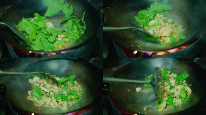 厨师在煎锅中用泰国圣罗勒烹调辛辣炒猪肉末的特写镜头，Pad Krapow是最受欢迎的泰国街头美食之一