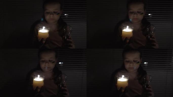 在黑暗的房间里，一个脸颊上挂着乌克兰国旗的女孩手里拿着蜡烛和电灯泡