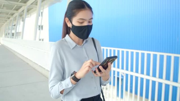 亚洲妇女使用手机，她戴着防护口罩，在建筑物外预防病毒，传染病。