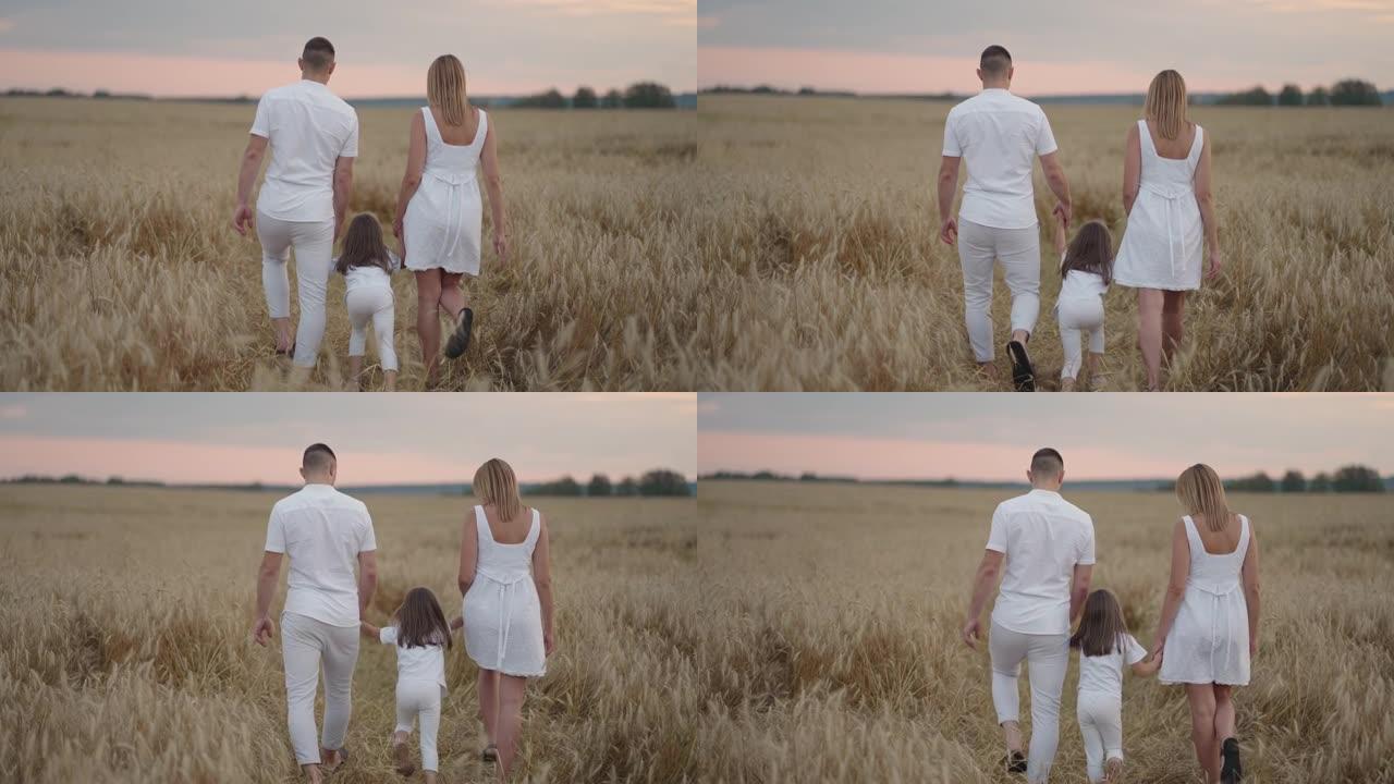 一对年轻的父母和女童手牵着手，在日落时分穿过麦田。幸福的家庭在大麦草地上慢跑，一起享受大自然。慢动作