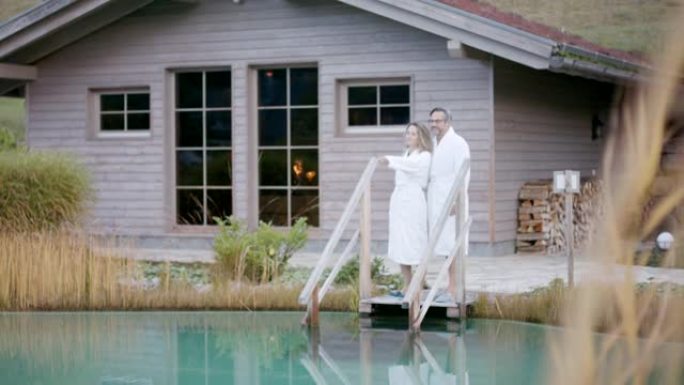 男人和女人站在池塘旁，穿着白色毛巾的桑拿浴室