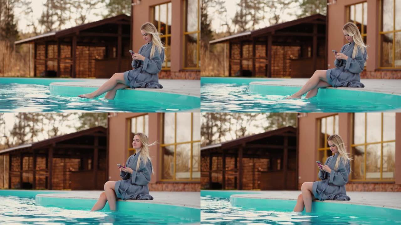 在温泉中心放松，年轻漂亮的女人在开放的游泳池附近休息，在温水中摇摆着腿
