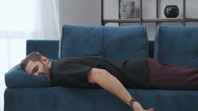 疲惫的男人倒在公寓的蓝色沙发上，慢动作，成年男人在家休息