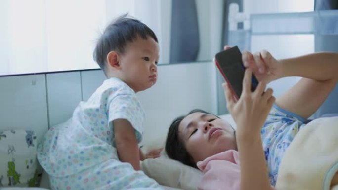 年轻的母亲和快乐的男婴 (12-23个月) 在家中使用智能手机