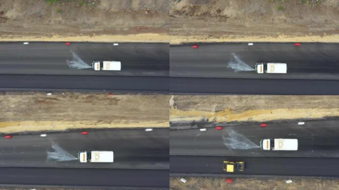 汽车在更新的柏油路路上泼水的空中镜头。道路工程后特种机械冲洗公路的俯视图。建设新高速公路的施工队。维