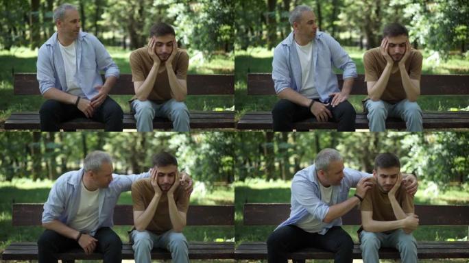 中年白人父亲支持悲伤的成年儿子的肖像。男人振作起来，紧张地坐在户外夏季公园的长凳上。支持和统一概念。