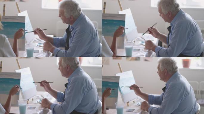 一位女老师向一位退休男子展示了如何在老年人课程中使用油漆和毛笔画画。一名高级男子为一群养老金领取者画