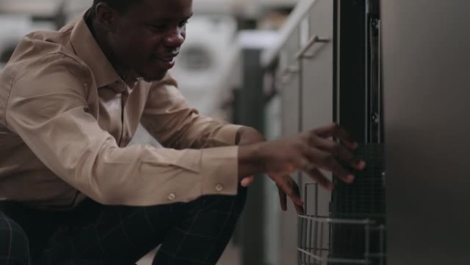 黑人正在购买家用厨房设备，年轻人正在家用电器商店看洗碗机
