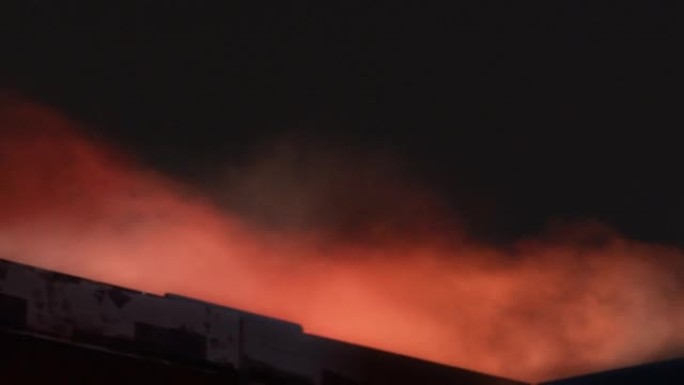 着火的家。建筑物上方的烟雾和红灯在黑暗的天空中