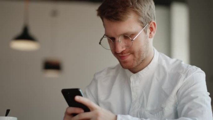 戴眼镜的有魅力的男人正在咖啡馆的智能手机显示屏上的社交媒体上观看有趣的图片和视频