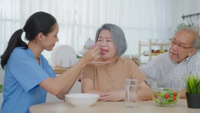 亚洲护理护士为有丈夫的老年女性患者提供食物。有吸引力的年轻专业护理女医生支持和照顾快乐的老年老奶奶在