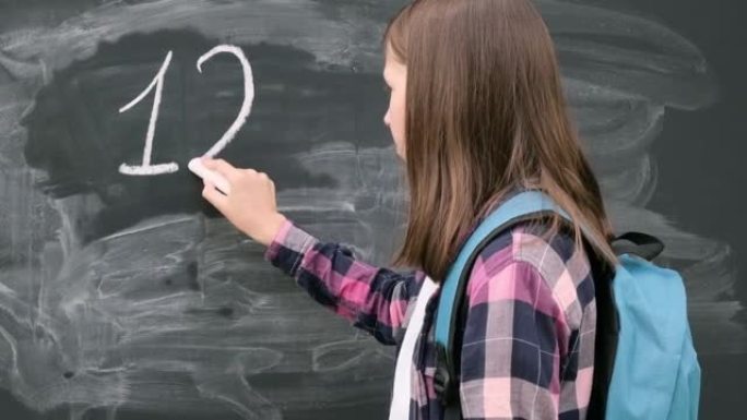 十几岁的学生女孩，穿着蓝色背包，用粉笔数字和字母写在黑色黑板背景上。教育，回到学校和人们的观念。黑板