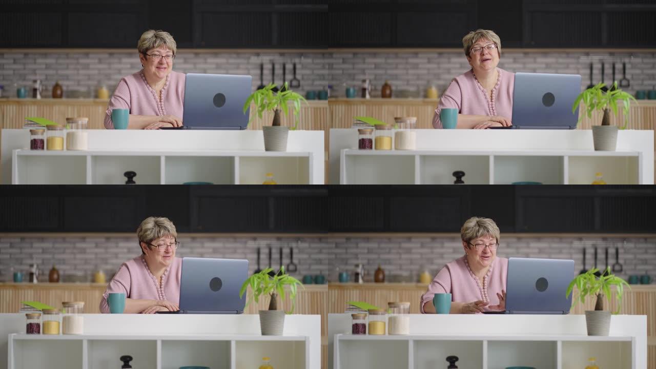 快乐的老年妇女通过笔记本电脑上的视频聊天进行交流，退休女士周末坐在家里的厨房里