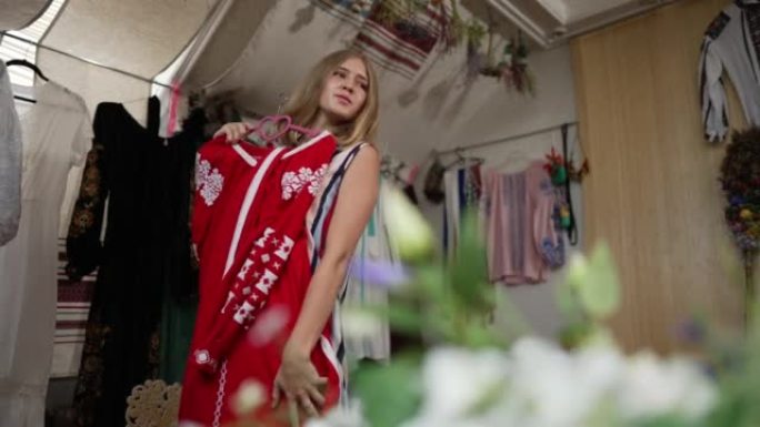 微笑的乌克兰少女在室内手工艺店选择传统刺绣连衣裙。迷人自信的青少年欣赏红色服装的肖像。风格和国籍。