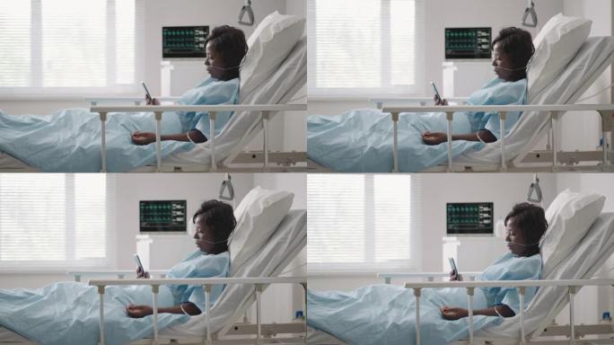 在医院用生理盐水溶液容积输液泵在检查沙发上使用手机的黑人妇女患者。非洲妇女在医院住院时躺在病床上，拿