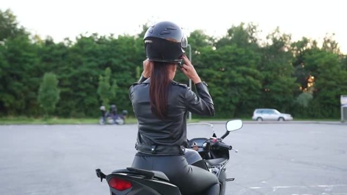穿着骑自行车的皮衣的未知迷人年轻时尚苗条的女人坐在豪华摩托车上，戴上防护头盔