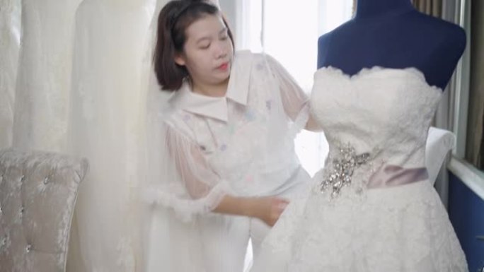 裁缝店老板婚纱室，在店里缝制一件白色婚纱。