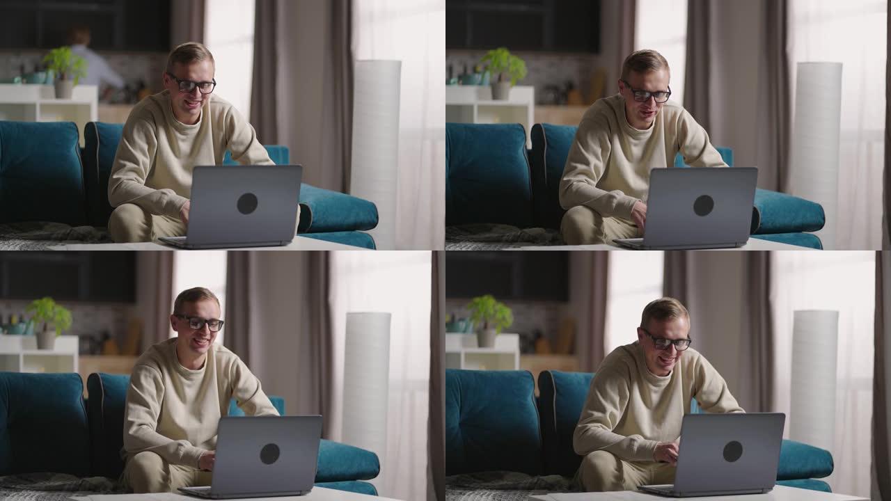男子坐在沙发上在家使用笔记本电脑进行视频隔离。快乐的年轻金发老师在家工作，在笔记本电脑视频会议上聊天