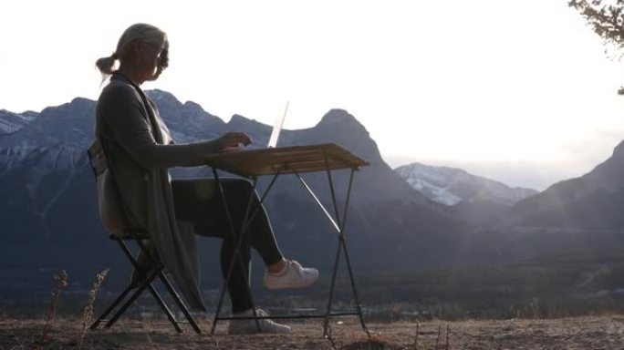 女人用笔记本电脑在野餐桌上放松，远处的山脉