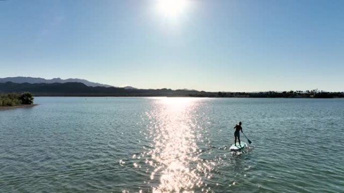 年轻女子在宁静的湖上站起来划水 (SUP) 的鸟瞰图