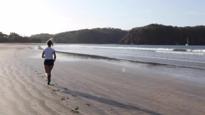 年轻女子沿着空旷的海滩奔跑，日出