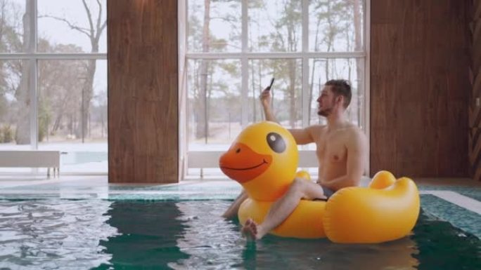 男子漂浮在酒店游泳池的充气圈上，并通过智能手机通过视频通话
