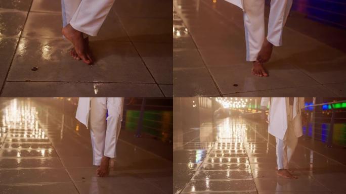 赤脚男子在潮湿的城市街道上表演自由式舞蹈。腿部特写
