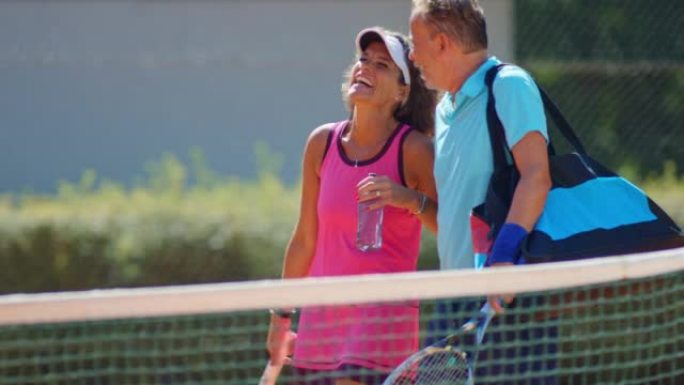 SLO MO TS中年夫妇在阳光明媚的网球场上漫步时会说话和大笑