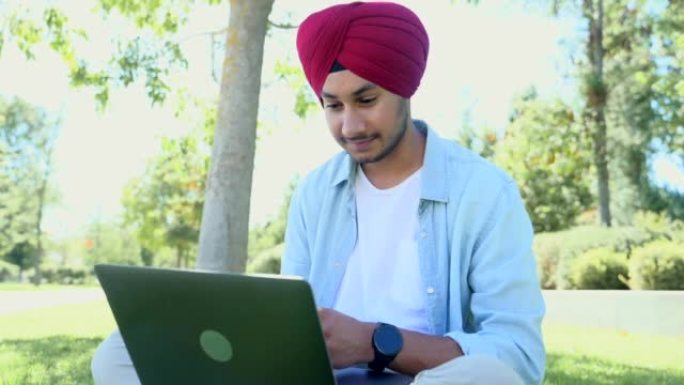 微笑和友好的印度教男性自由职业者戴着国家头巾，使用笔记本电脑进行视频会议