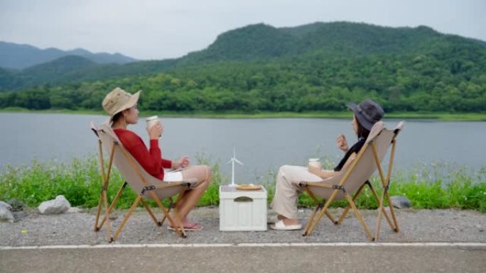 亚洲女孩坐在野营椅上，吃喝，在与大自然放松的一天放松。