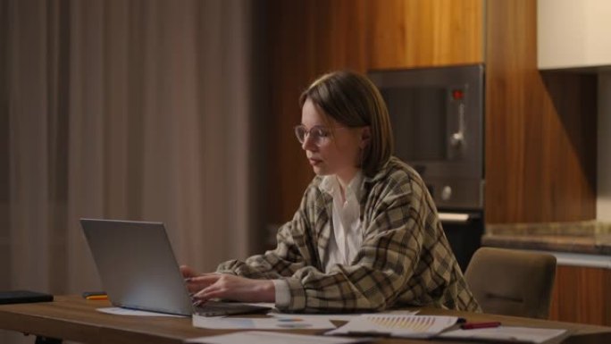 女孩在家工作或学生在家学习或自由职业者。她使用笔记本电脑和电话。女孩坐在客厅的桌子上，在笔记本电脑上