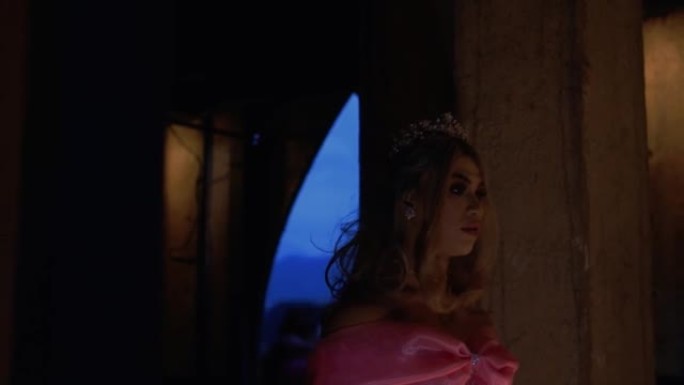 一位穿着粉红色连衣裙的公主戴着皇冠和头饰在黑暗中缓慢行走