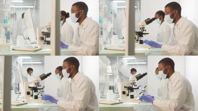 带有显微镜的非洲民族科学家。背景中的计算机屏幕。他身后忙碌的团队