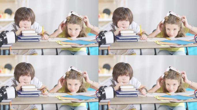 不高兴的高加索男孩和无聊的女孩坐在课桌上看着相机。不幸的孩子在学校学习的肖像。无聊和教育。