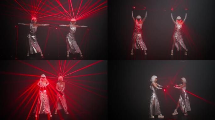 穿着红色霓虹灯在黑色背景下跳舞的服装中，自信的女表演者同时移动。苗条的专业高加索舞者用激光束在舞台上